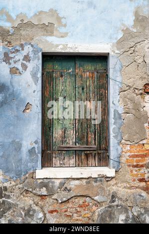 Une vieille fenêtre à volet en bois dans un mur de plâtre exposé à Venise Italie. Banque D'Images