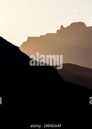 La dernière lumière du soleil couchant brille à travers une vallée et les montagnes des montagnes du Drakensberg central en Afrique du Sud Banque D'Images
