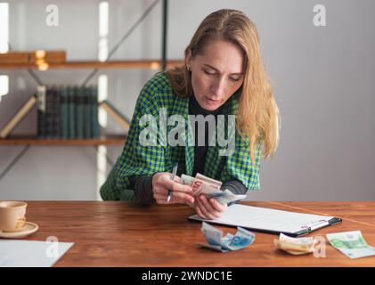 Une jeune jolie dame est réfléchie et réfléchie à compter l'argent pour un projet. Banque D'Images