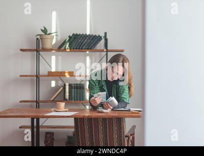 Une jeune jolie dame compte l'argent de façon réfléchie et attentive dans son bureau à domicile. Banque D'Images