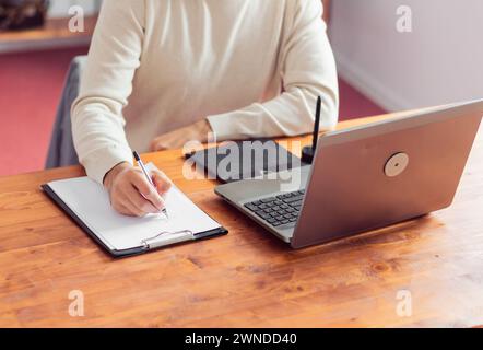 Un graphiste au bureau fait un croquis avec un crayon sur papier et travaille sur un ordinateur portable et une tablette graphique. L'accent est mis sur la main, tout els Banque D'Images