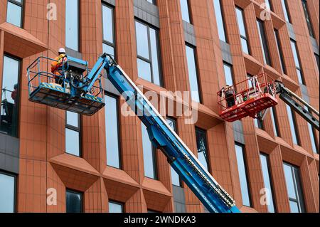 Ouvriers de la construction sur des plates-formes surélevées apportant la touche finale aux fenêtres Banque D'Images