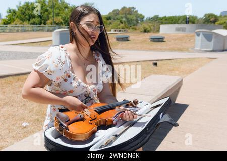 Jeune femme violoniste de busker latina, assise mettant son violon en cas après avoir travaillé dans la rue comme artiste de rue à Buenos Aires, copier l'espace. Banque D'Images