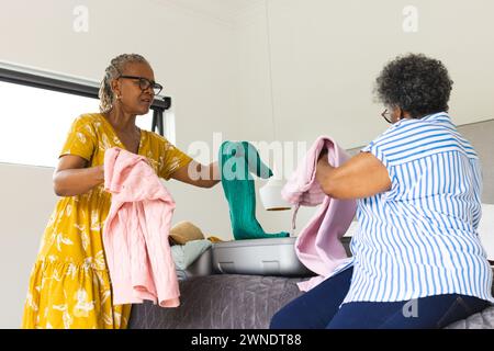 Femme afro-américaine senior et femme biraciale plient des vêtements ensemble, emballant une valise Banque D'Images