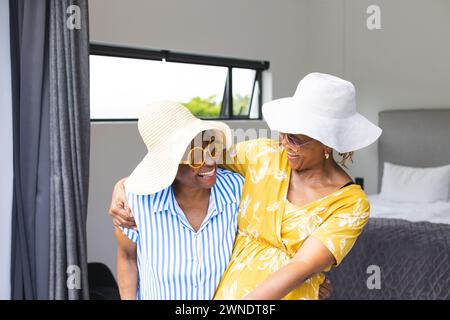 Femme afro-américaine senior et femme biraciale porter des chapeaux de soleil élégants et des lunettes de soleil en vacances Banque D'Images