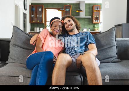 Couple diversifié jeune femme afro-américaine et homme caucasien assis étroitement sur un canapé, souriant chaleureusement Banque D'Images