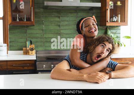 Joyeux couple diversifié partage un rire dans une cuisine lumineuse. Banque D'Images