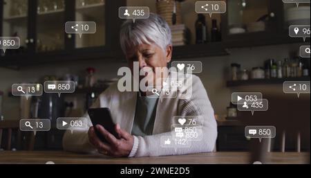 Image des icônes de médias sociaux et des numéros sur les bannières sur la femme senior à l'aide d'un smartphone Banque D'Images