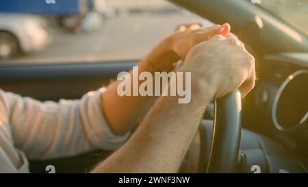 Fermez les mains masculines tournant le volant conduisant le véhicule dans les rayons de soleil de coucher du soleil homme d'affaires propriétaire d'auto de voiture de ville route de coupe croisée conducteur de tir Banque D'Images