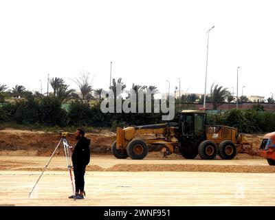 Le Caire, Égypte, 23 février 2024 : un ingénieur et un nivellement du sol avec un camion niveleur et un niveleur laser en train de paver une route avant de faire asph Banque D'Images