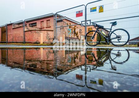 Vélo de route spécialisé Roubaix Expert s'est tenu contre une clôture métallique près d'un bâtiment abandonné grungy avec une flaque reflétant la scène, pays de Galles, Royaume-Uni Banque D'Images