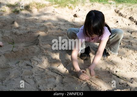 Fille asiatique jouant dans le sable à l'aire de jeux dans le parc. Banque D'Images