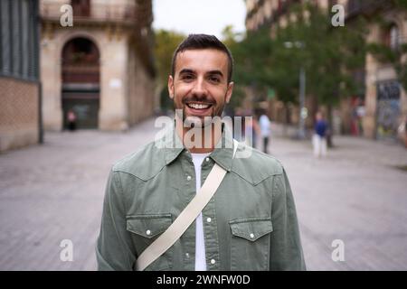 Portrait jeune homme barbu beau se tient regardant la caméra souriant dans la rue dans la ville de Barcelone. Banque D'Images