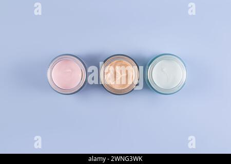 Trois beaux pots cosmétiques en verre avec une texture délicate de crème de soins pour le visage et le corps sur un fond bleu. Vue de dessus. Un espace de copie. présentation Banque D'Images