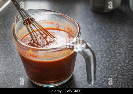 Remuer la sauce rouge enchilada dans un pot de mesure en verre. Banque D'Images