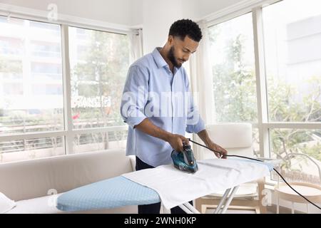 Jeune homme afro-américain propriétaire repassage serviette en tissu Banque D'Images