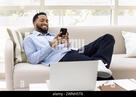 Joyeux homme freelance africain détendu reposant sur le canapé du bureau à la maison Banque D'Images