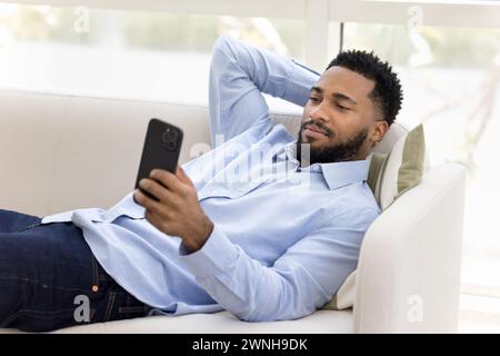 Détendu jeune homme noir dans la chemise de bureau couché sur le canapé Banque D'Images