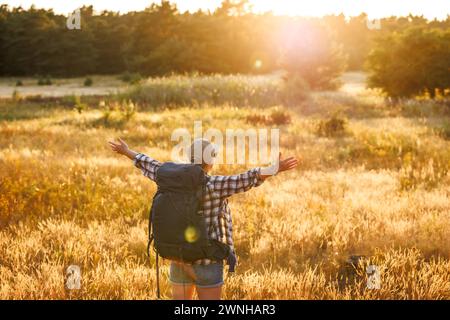 Joyeux randonneur solo profitant du coucher du soleil pendant le trekking dans la nature. Femme avec sac à dos randonnée en été Banque D'Images