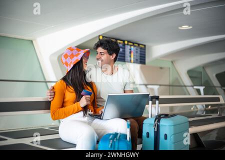 couple avec carte de crédit se regardant amoureux à l'aéroport après avoir acheté leur billet avec l'ordinateur portable Banque D'Images