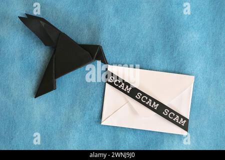 Noir corbeau papier origami portant une enveloppe de lettre blanche avec mot arnaque. Concept de message d'arnaque. Banque D'Images
