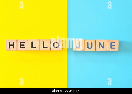 Bonjour le concept du mois de juin. Typographie de blocs en bois en fond bleu vif et jaune. Banque D'Images