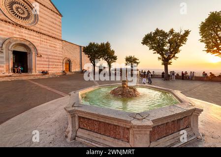 Fontaine sur la place St Clare en face de la basilique au coucher du soleil doré dans la vieille ville d'assise, Ombrie, Italie Banque D'Images