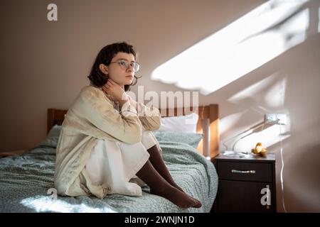 Une adolescente introvertie s'assoit sur le lit dans une humeur apathique, pensant aux problèmes, à l'intimidation à l'école Banque D'Images