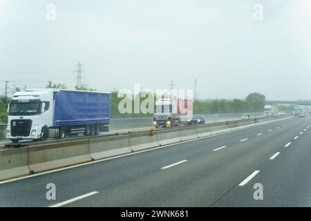 Parme, Italie - 10 mai 2023 : les camions roulent dans des directions opposées sur une autoroute humide, avec de l'eau pulvérisée par les roues en raison de la pluie. Banque D'Images