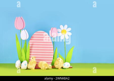 Fleurs de printemps et oeuf de Pâques en bois avec des poussins devant un fond bleu Banque D'Images