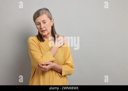 Symptômes de l'arthrite. Femme souffrant de douleur au coude sur fond gris, espace pour le texte Banque D'Images