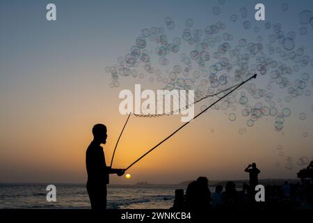 Un homme en silhouette fait beaucoup de bulles de savon avec un bâton de bulle de savon, ils flottent dans le ciel orange au coucher du soleil, certaines personnes en silhouette regardent dessus Banque D'Images
