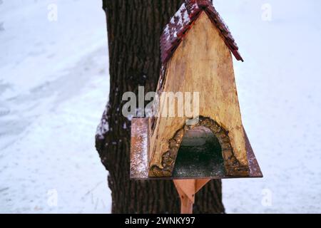 Mangeoire à oiseaux sur un arbre sous la forme d'une maison. Mangeoire pour écureuils et oiseaux sur un arbre en hiver Banque D'Images