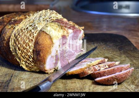 Un gros morceau de jambon, un couteau et des tranches de viande hachée reposent sur une planche à découper. Banque D'Images