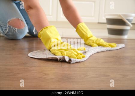 Une femme lave le sol avec ses mains dans une cuisine à domicile, travail manuel. Les mains des femmes en gants jaunes lors du nettoyage de la cuisine Banque D'Images