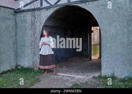 Une ancienne maison et une femme dans une robe vintage à côté d'une arcade menant à une cour Banque D'Images