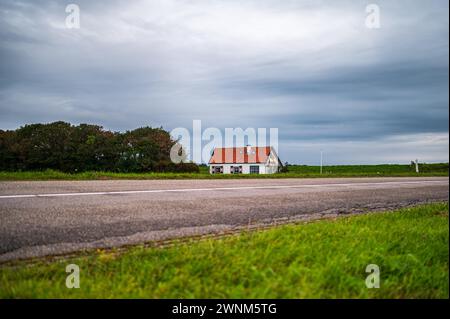 Maison solitaire à côté d'une route sous un ciel nuageux au crépuscule, transmet la paix et l'isolement, Texel, Noord-Holland, pays-Bas Banque D'Images