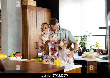 La famille partage un sourire tout en préparant le petit déjeuner ensemble dans une cuisine confortable et bien éclairée Banque D'Images