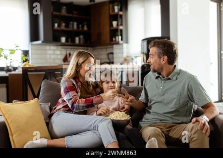 Un joyeux salon familial sur le canapé, s'engageant dans une conversation ludique avec un bol de pop-corn Banque D'Images