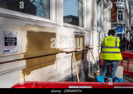 Londres, Royaume-Uni. 3 mars 2024. Un travailleur de la construction couvre les créneaux pour les distributeurs automatiques de billets et d'autres installations dans une ancienne succursale de la banque NatWest sur Chiswick High Road dans l'ouest de Londres. Alors que les banques migrent principalement vers des services en ligne et ferment des succursales physiques pour économiser de l'argent, les critiques disent que certains membres de la communauté sont laissés pour compte car ils dépendent de l'argent liquide, n'ont pas accès aux services bancaires en ligne et préfèrent un contact face à face avec le personnel de leur succursale locale. Credit : Stephen Chung / Alamy Live News Banque D'Images