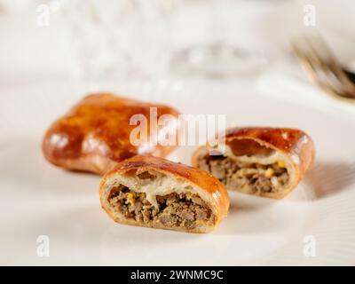 Petites tartes russes à la viande hachée Piroshki russe. Tartes ou empanadas découpées en deux sur une assiette blanche à la viande cuite dans l'élégant intérieur du restaurant. Mise au point sélective, gros plan. Banque D'Images