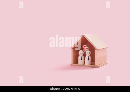 Joyeuses figures de famille gay en bois à l'intérieur d'une minuscule maison en bois isolée sur un fond rose. Deux hommes de fierté souriant et se tiennent proches l'un de l'autre Banque D'Images