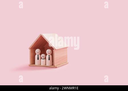 Joyeuses figures de famille gay en bois à l'intérieur d'une minuscule maison en bois isolée sur un fond rose. Deux pères fiers et un enfant souriant se tiennent proches l'un de l'autre Banque D'Images