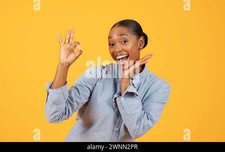 Femme afro-américaine montre un geste de main OK sur fond jaune Banque D'Images