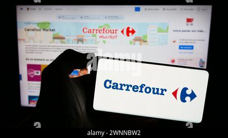 Personne tenant un smartphone avec le logo de la société française Carrefour S.A. en face du site. Concentrez-vous sur l'affichage du téléphone. Banque D'Images