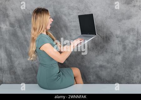 Belle femme blonde assise sur une table travaillant avec un ordinateur portable à la maison Banque D'Images