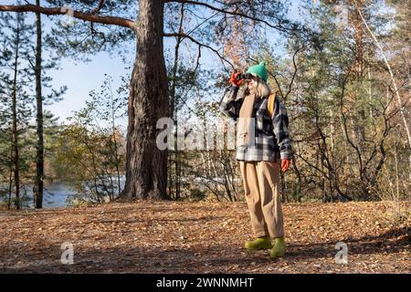 Focalisé intéressée femme touriste ornithologue debout dans la forêt regardant à travers des jumelles sur les oiseaux. Banque D'Images
