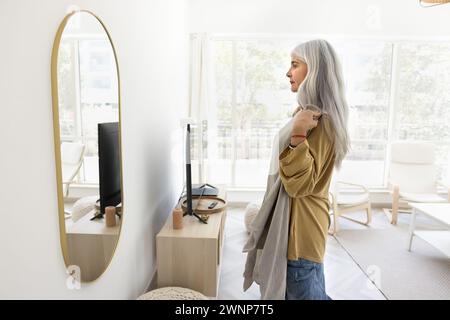 Sérieuse femme latine âgée aux cheveux gris essayant sur le tissu Banque D'Images