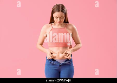 Bouleversée jeune femme en jeans serrés sur fond rose. Concept de gain de poids Banque D'Images