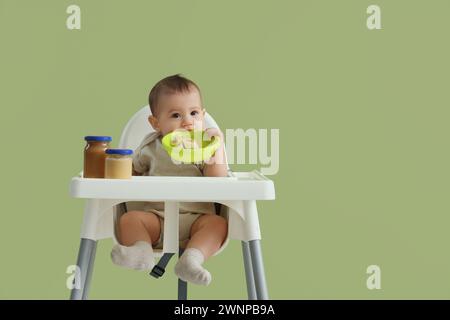 Petit bébé mignon avec bol de banane à la table d'alimentation sur fond vert Banque D'Images